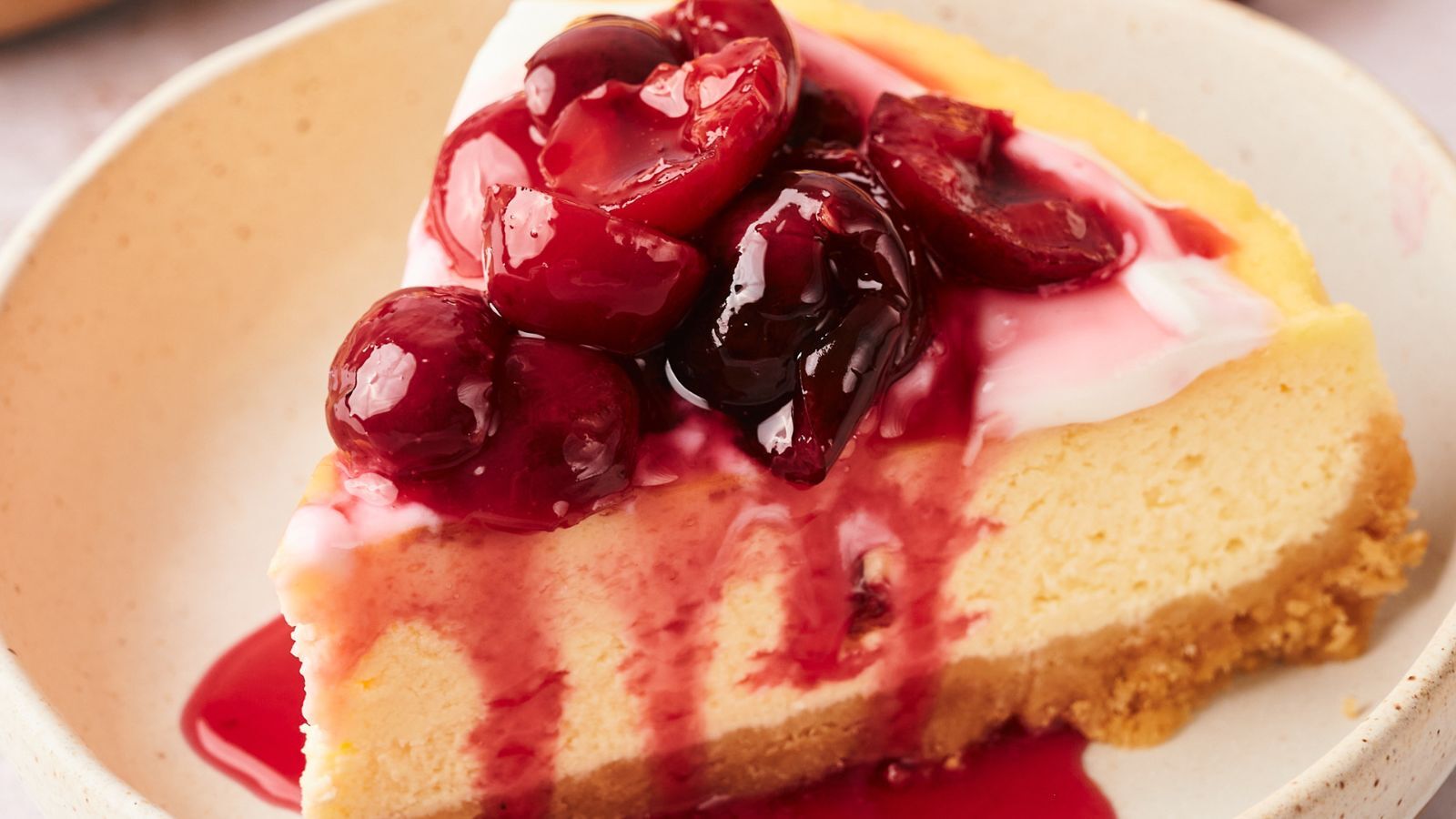 A slice of cheesecake topped with cherry sauce, sitting on a beige plate.