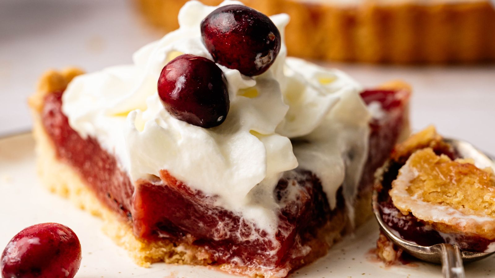 A slice of cherry pie topped with whipped cream and whole cherries sits on a plate, with a fork holding a bite-sized piece nearby.