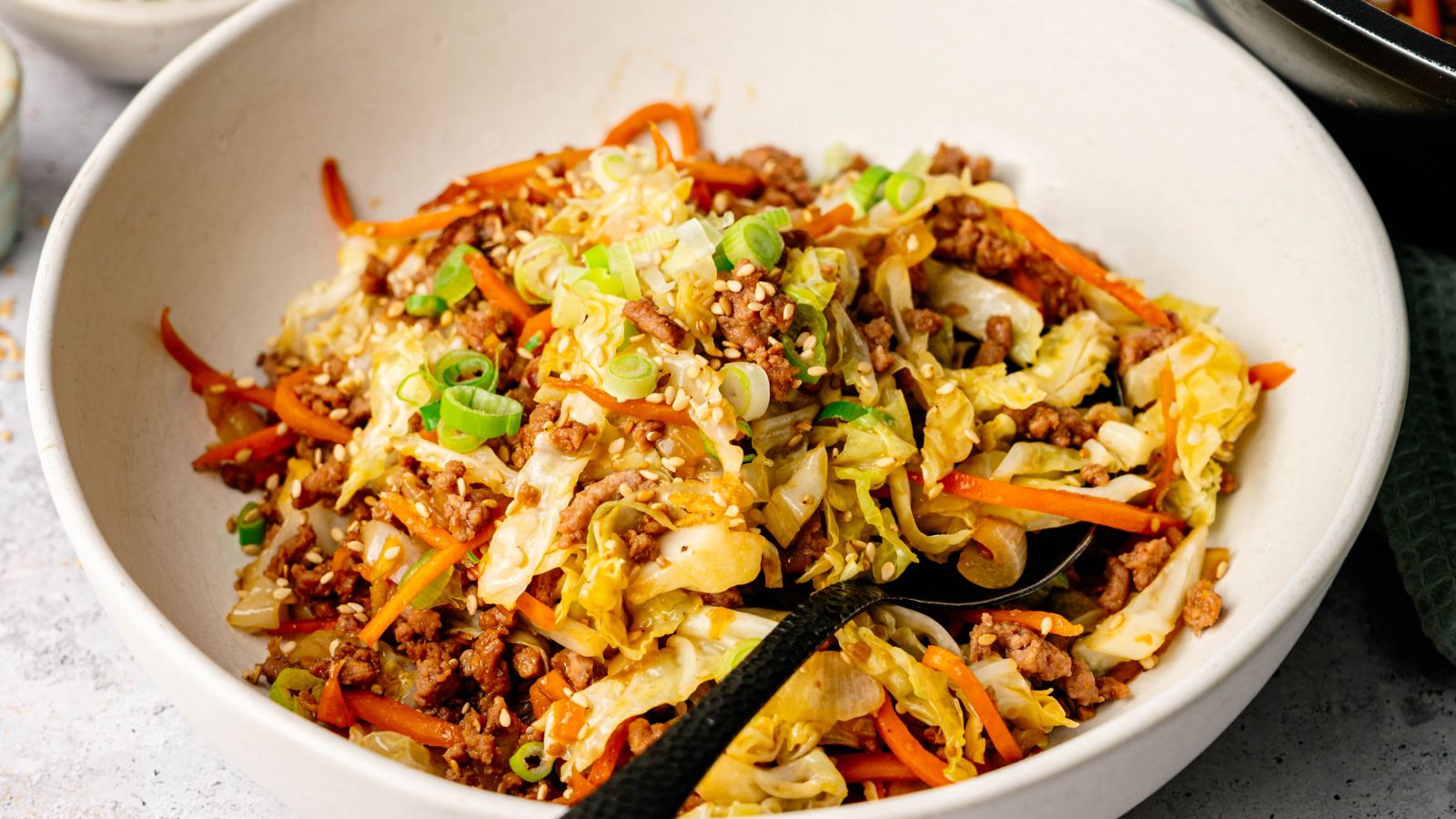 A bowl of stir-fried ground meat, shredded cabbage, and carrots, topped with sesame seeds and chopped green onions.