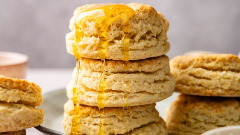 A stack of fluffy biscuits with honey drizzled over the top, placed on a plate.