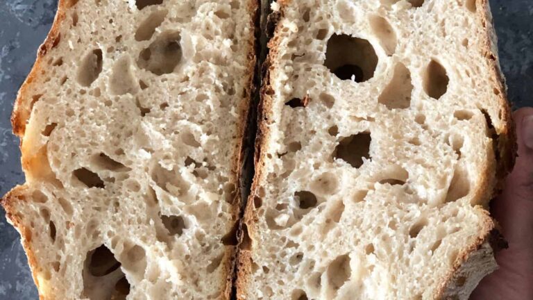 A close-up of a sliced loaf of sourdough bread, showing an airy, open crumb structure and a golden crust.