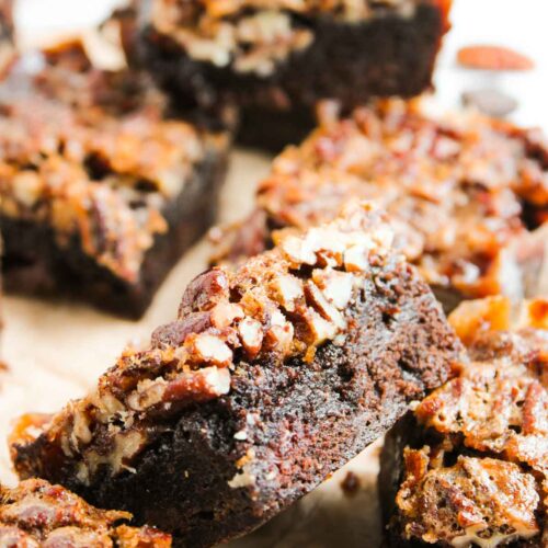 Close-up of several Pecan Pie Brownies topped with chopped pecans, arranged on a piece of parchment paper.