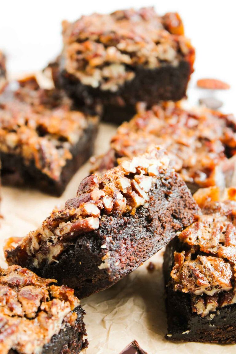 Close-up of several Pecan Pie Brownies topped with chopped pecans, arranged on a piece of parchment paper.