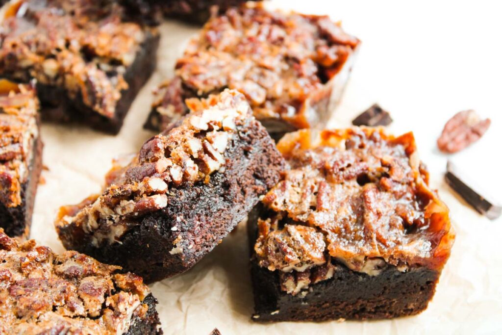 Close-up of several Pecan Pie Brownies, showcasing a rich, fudgy base topped with a layer of pecans and caramelized topping on parchment paper.