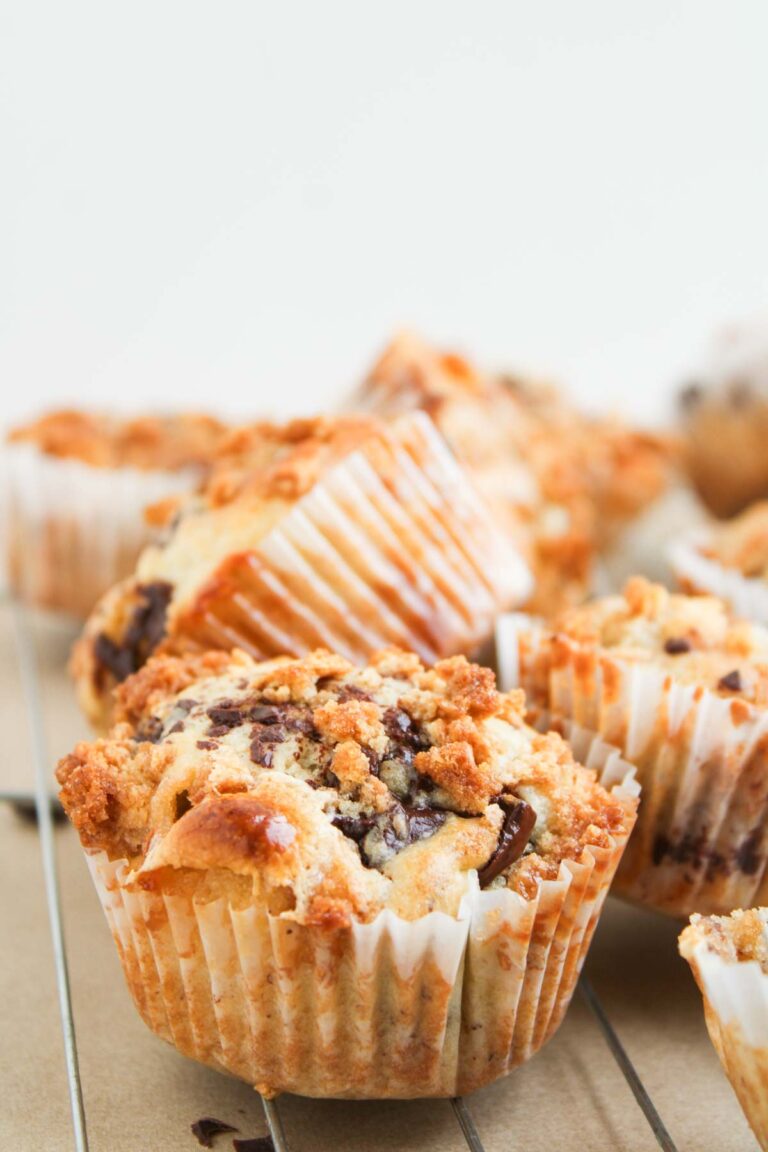 S'mores Muffins with chocolate chips and crumb topping cool on a wire rack in white paper liners, set against a plain background.