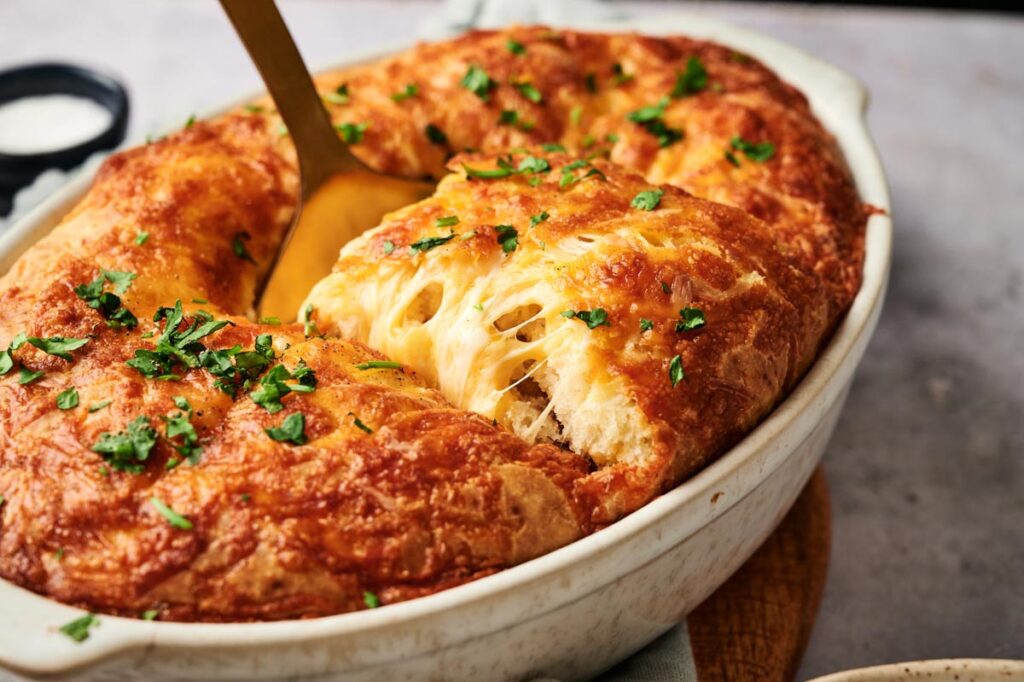 A baked Sloppy Joe Casserole dish with a golden, cheesy crust being served, garnished with chopped parsley.
