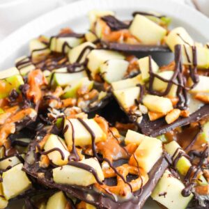 A plate of Caramel Apple Bark topped with chopped green apples, pretzel pieces, caramel drizzle, and dark chocolate drizzle.