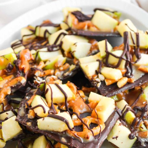 A plate of Caramel Apple Bark topped with chopped green apples, pretzel pieces, caramel drizzle, and dark chocolate drizzle.