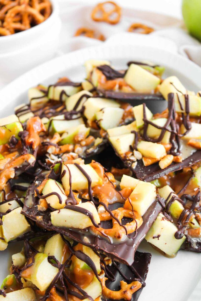 A plate of Caramel Apple Bark topped with chopped green apples, pretzel pieces, caramel drizzle, and dark chocolate drizzle.