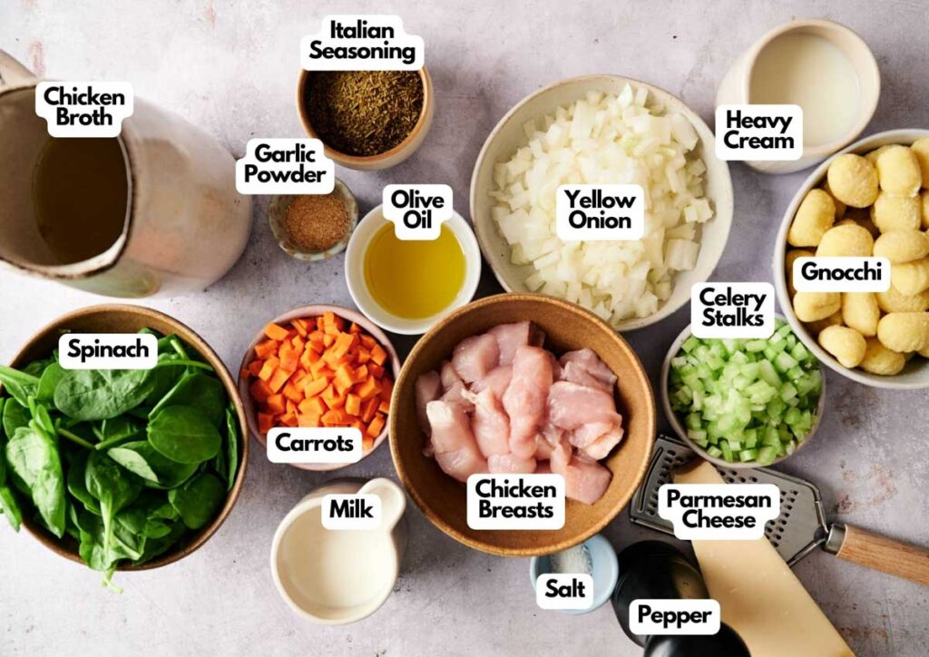 Bowls and cups containing labeled ingredients for Chicken Gnocchi Soup&mdash;including chicken breasts, vegetables, gnocchi, seasonings, dairy, broth, and olive oil&mdash;are neatly arranged on a countertop.