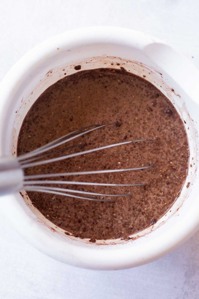 A metal whisk rests in a white mixing bowl filled with rich Chocolate Chia Pudding batter.
