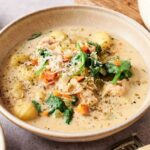 A bowl of creamy Chicken Gnocchi Soup with spinach, carrots, herbs, grated cheese, and tender pieces of chicken.