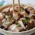 A bowl of Chinese Steamed Chicken pieces with mushrooms, garnished with chopped green onions, with chopsticks picking up a tender bite.