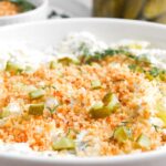 A close-up of Fried Dill Pickle Dip, a creamy dip topped with breadcrumbs, chopped pickles, and fresh dill in a white bowl.