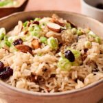 A bowl of Rice Pilaf topped with sliced green onions, whole almonds, and dried cranberries.
