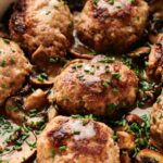 Several browned Salisbury Steak patties in a creamy mushroom sauce, garnished with chopped chives.