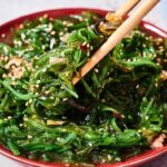 A plate of Seaweed Salad garnished with sesame seeds, with chopsticks lifting a fresh, flavorful portion.