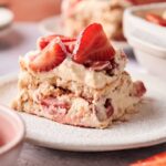 A slice of Strawberry Tiramisu with layers of cream, ladyfingers, and fresh strawberries is beautifully served on a white plate.