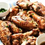 Plate of grilled turkey wings garnished with chopped herbs, served with small bowls of sauce and extra herbs on the side.