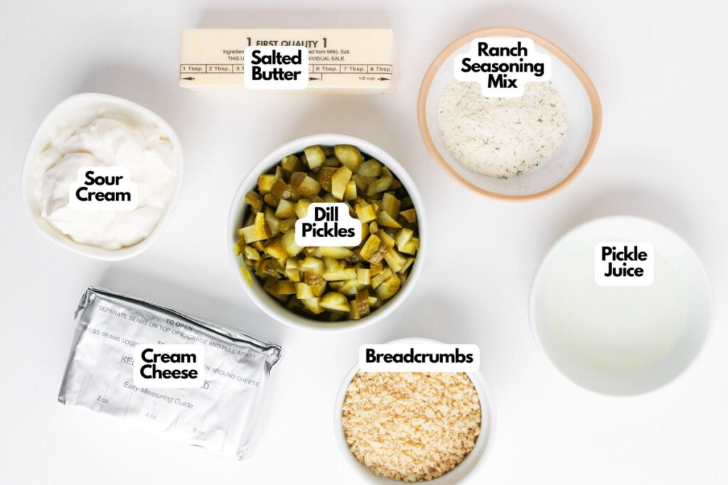 Top-down view of labeled ingredients in bowls for Fried Dill Pickle Dip: sour cream, salted butter, ranch seasoning mix, dill pickles, pickle juice, cream cheese, and breadcrumbs on a white surface.