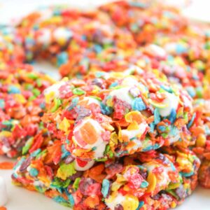 Close-up of colorful Fruity Pebble Rice Krispies bars made with marshmallows, stacked neatly on a white surface.