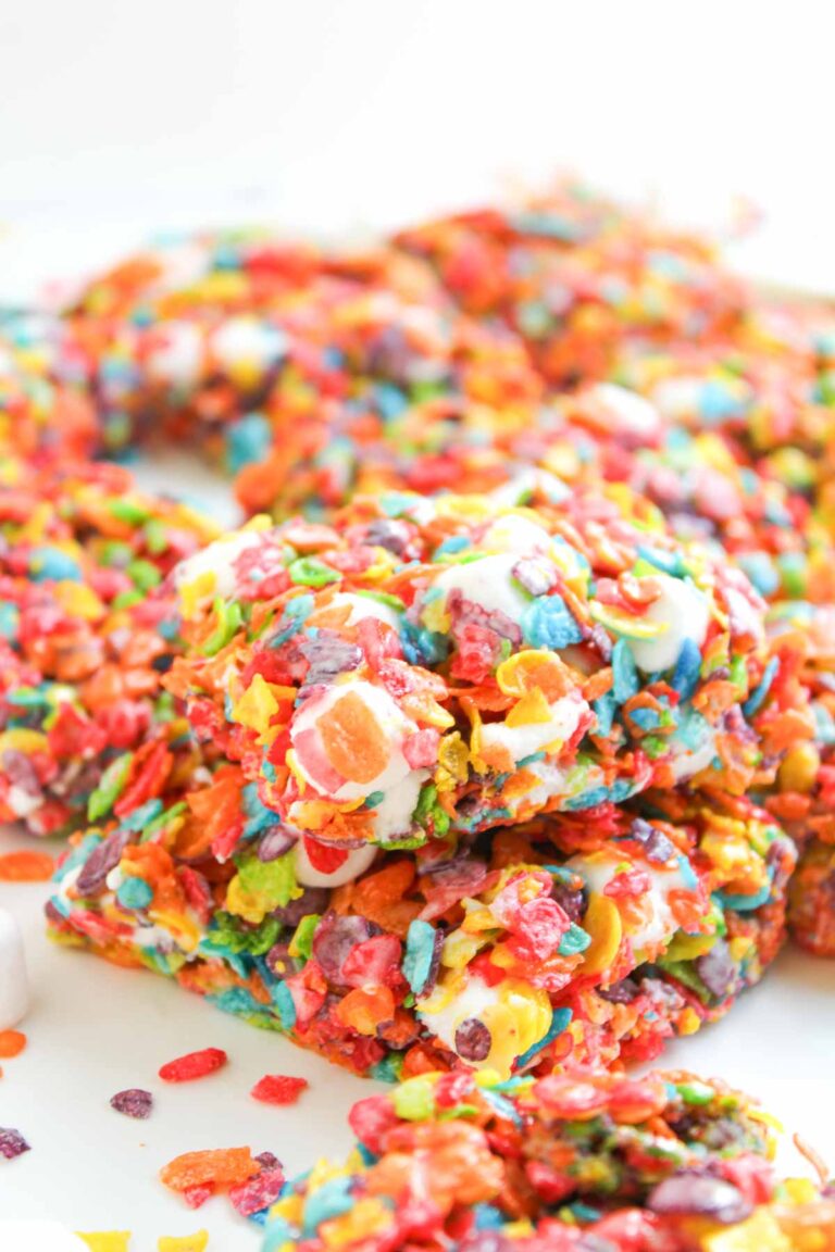 Close-up of colorful Fruity Pebble Rice Krispies bars made with marshmallows, stacked neatly on a white surface.