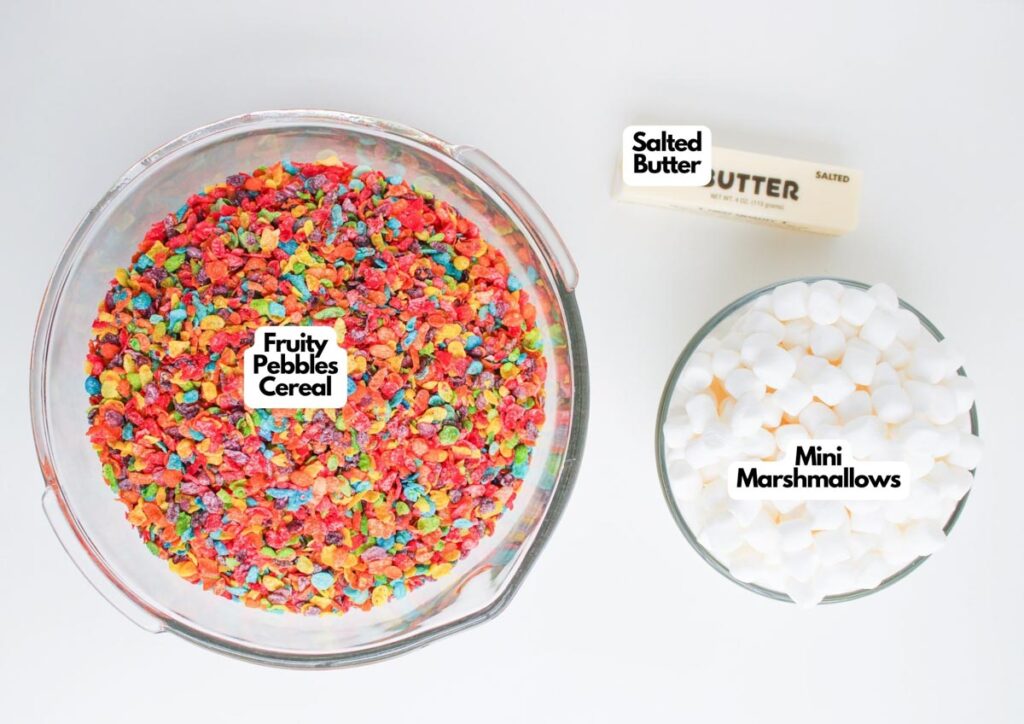 A bowl of Fruity Pebbles cereal, a bowl of mini marshmallows, and a stick of salted butter are arranged on a white surface, each labeled&mdash;perfect for making colorful Fruity Pebble Rice Krispies treats.