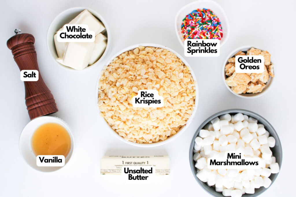 Top-down view of Funfetti Rice Krispie Treats ingredients in bowls: Rice Krispies, mini marshmallows, white chocolate, butter, golden Oreos, rainbow sprinkles, vanilla, and a salt grinder.