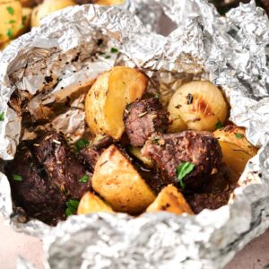 Chunks of beef and roasted potatoes in a Garlic Butter Steak and Potatoes Foil Packet, seasoned with herbs and garnished with chopped parsley.