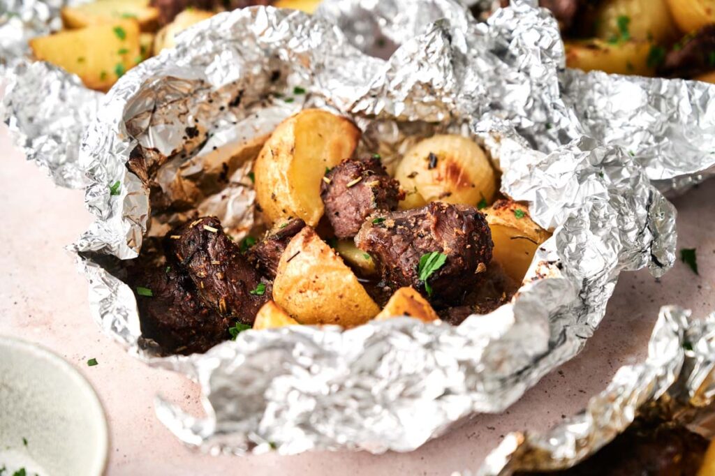Garlic Butter Steak and Potatoes Foil Packet featuring cooked beef chunks and roasted potatoes, garnished with chopped herbs, presented on a light-colored surface.