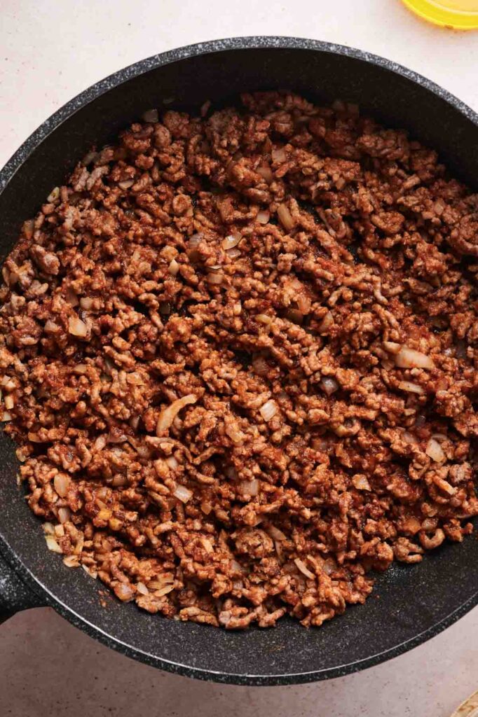 Cooked ground beef with chopped onions and spices in a black skillet, perfect for filling a tasty Grilled Cheese Burrito.