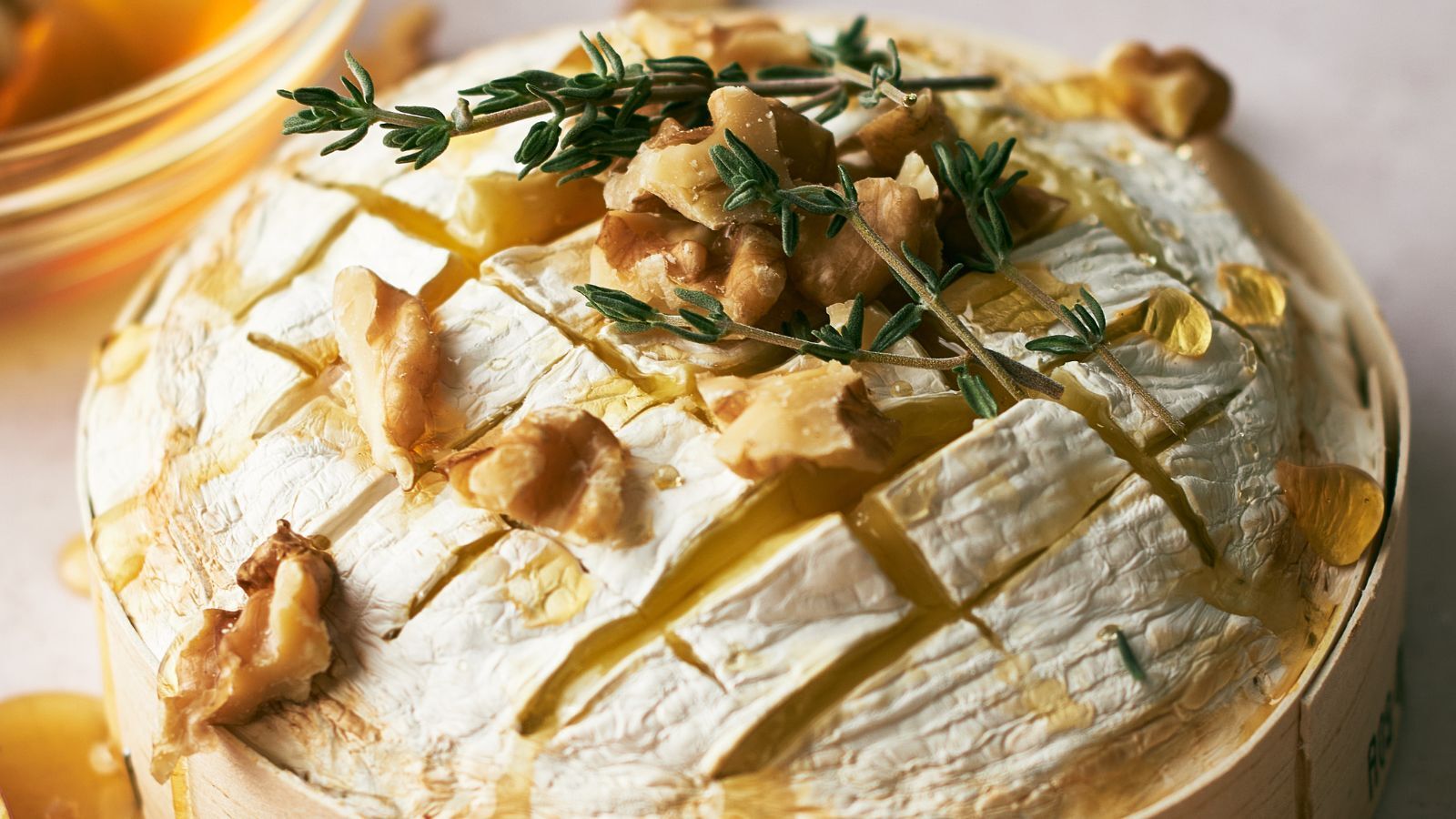 Round baked brie cheese topped with walnuts, fresh thyme, and drizzled honey, served in a wooden container.