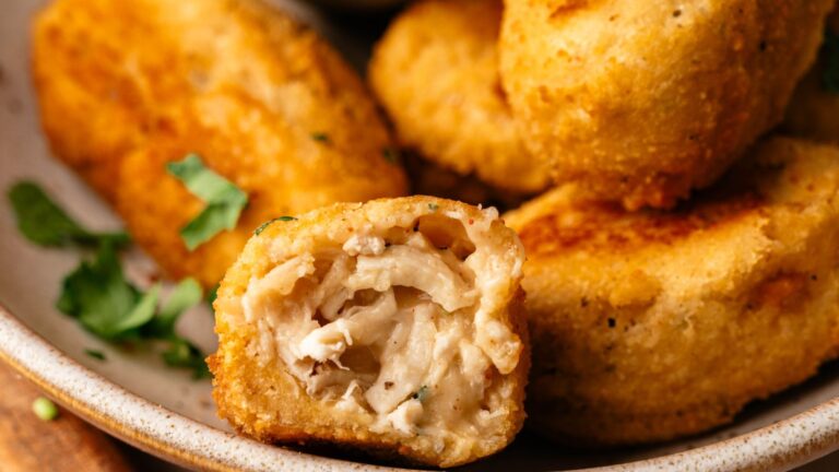 Close-up of several breaded chicken nuggets on a plate, with one nugget cut open to show the shredded chicken filling inside.