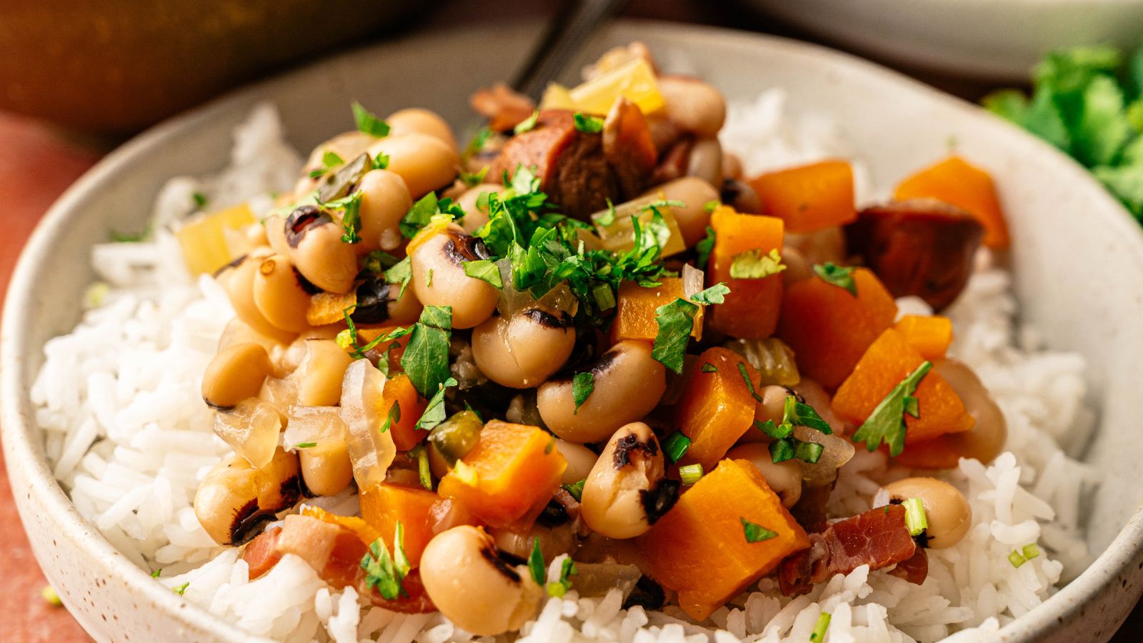 A bowl of white rice topped with black-eyed peas, diced sweet potatoes, onions, herbs, and chopped parsley.