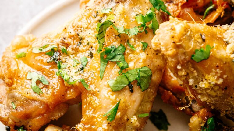 Close-up of seasoned and baked chicken wings garnished with chopped fresh herbs on a white plate.