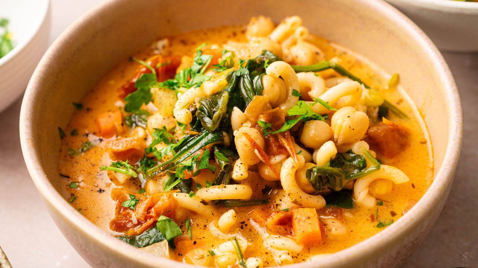 A bowl of pasta soup with chickpeas, spinach, tomatoes, and herbs in a creamy broth.