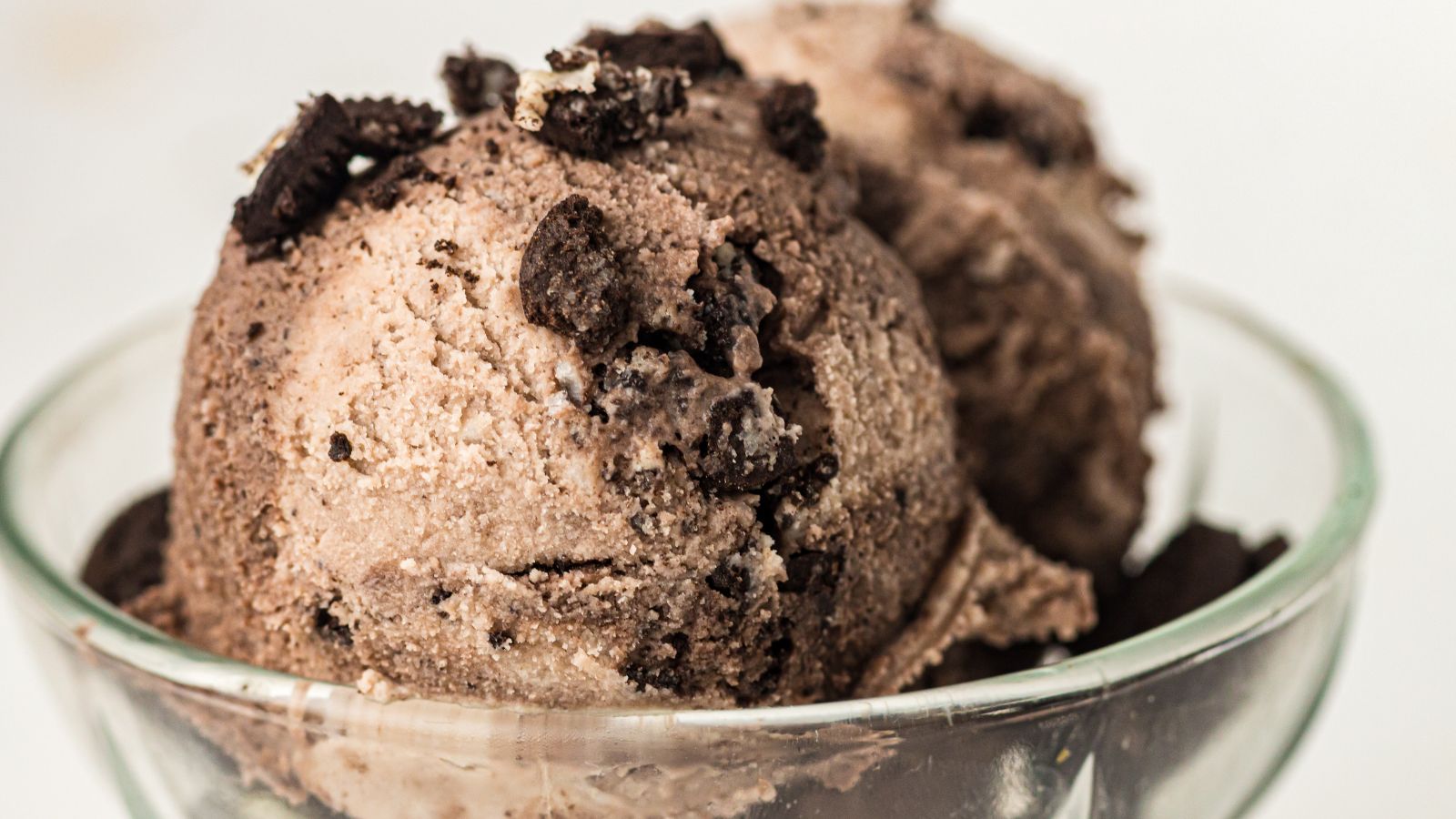 Two scoops of chocolate ice cream with crumbled chocolate cookies on top, served in a clear glass bowl.