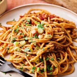 A plate of Mexican Spaghetti with savory meat sauce, garnished with chopped green onions and herbs, served on a beige plate with a black fork.