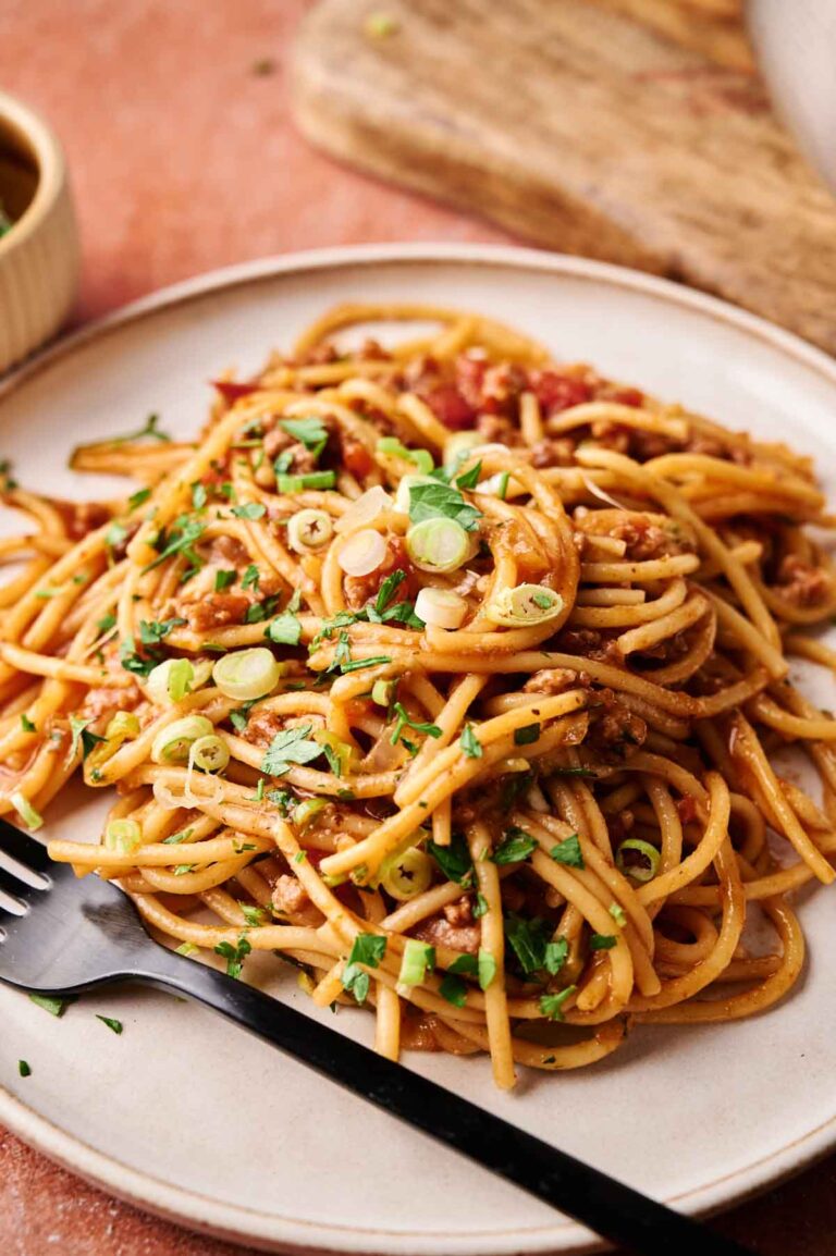 A plate of Mexican Spaghetti with savory meat sauce, garnished with chopped green onions and herbs, served on a beige plate with a black fork.