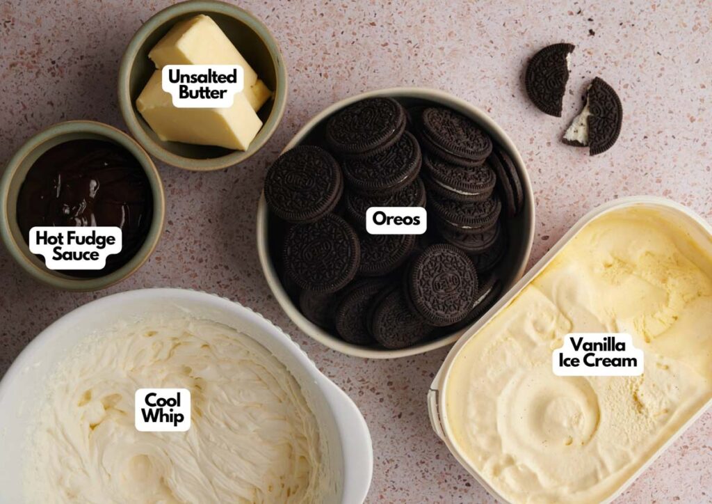 Bowls containing unsalted butter, hot fudge sauce, Oreos, vanilla ice cream, and Cool Whip are arranged on a countertop—perfect ingredients for an irresistible Oreo Ice Cream Cake.