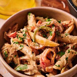 A bowl of Rasta Pasta with penne, sliced bell peppers, and creamy sauce, garnished with chopped fresh herbs.