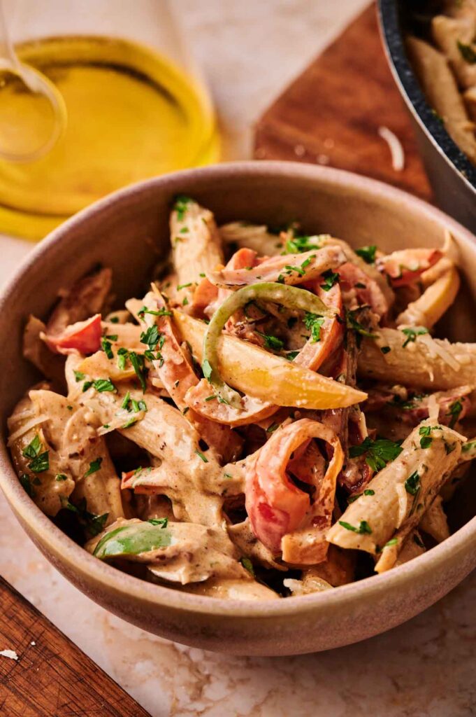 A bowl of Rasta Pasta with penne, sliced bell peppers, and creamy sauce, garnished with chopped fresh herbs.