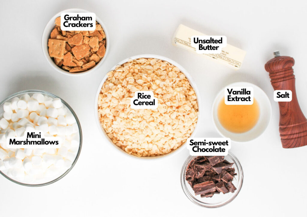 Top-down view of S'mores Rice Krispies ingredients in bowls and containers: graham crackers, rice cereal, mini marshmallows, unsalted butter, vanilla extract, semi-sweet chocolate, and salt.