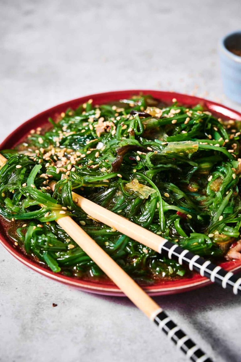A fresh plate of Seaweed Salad topped with sesame seeds, served with a pair of chopsticks on a gray surface.
