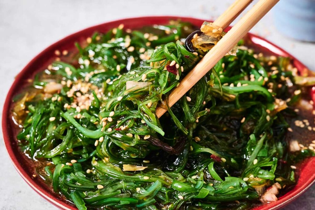 A plate of Seaweed Salad garnished with sesame seeds, with chopsticks picking up a fresh, flavorful portion.