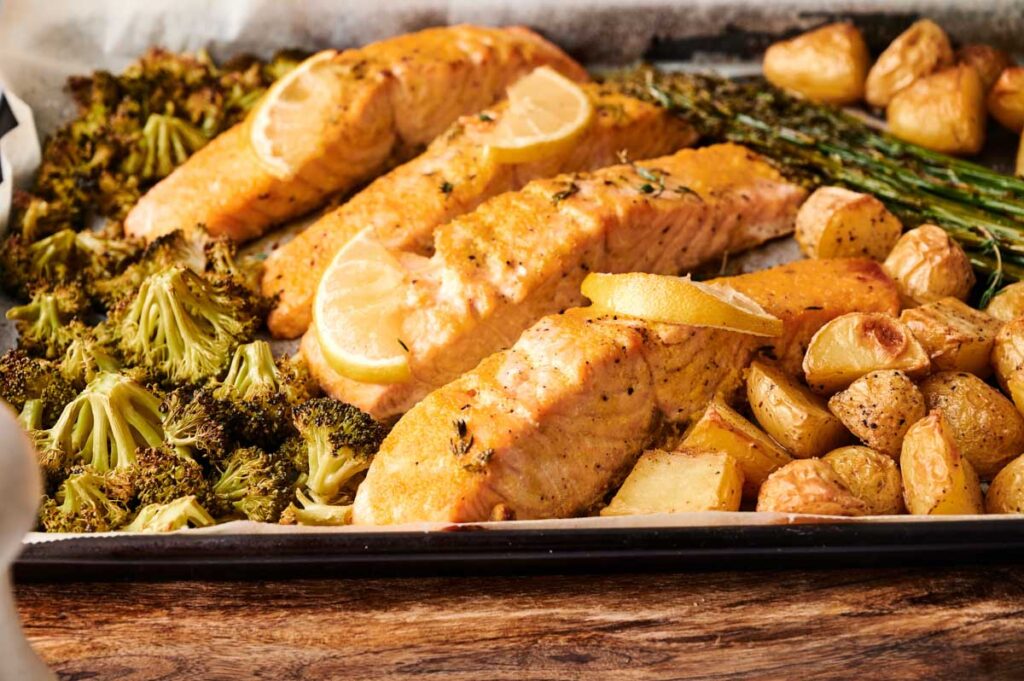 Sheet Pan Salmon fillets baked with lemon slices, surrounded by roasted broccoli, asparagus, and potatoes&mdash;all perfectly arranged on a single pan for an easy, delicious meal.