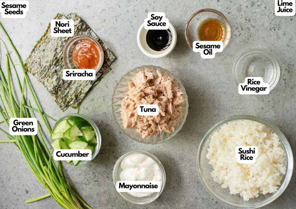 Overhead view of ingredients for a Spicy Tuna Bowl, including tuna, sushi rice, nori, cucumber, green onions, sesame seeds, sriracha, mayonnaise, soy sauce, sesame oil, vinegar, and lime juice.