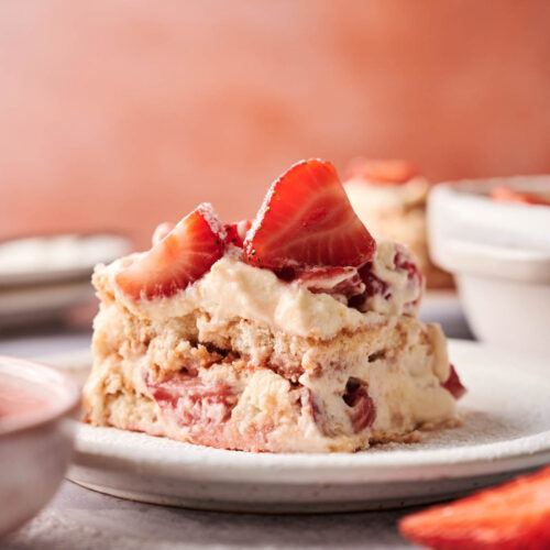 A slice of Strawberry Tiramisu is served on a white plate, topped with fresh strawberry slices.