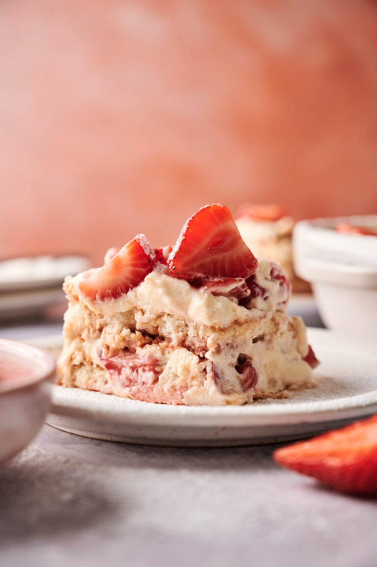 A slice of Strawberry Tiramisu is served on a white plate, topped with fresh strawberry slices.