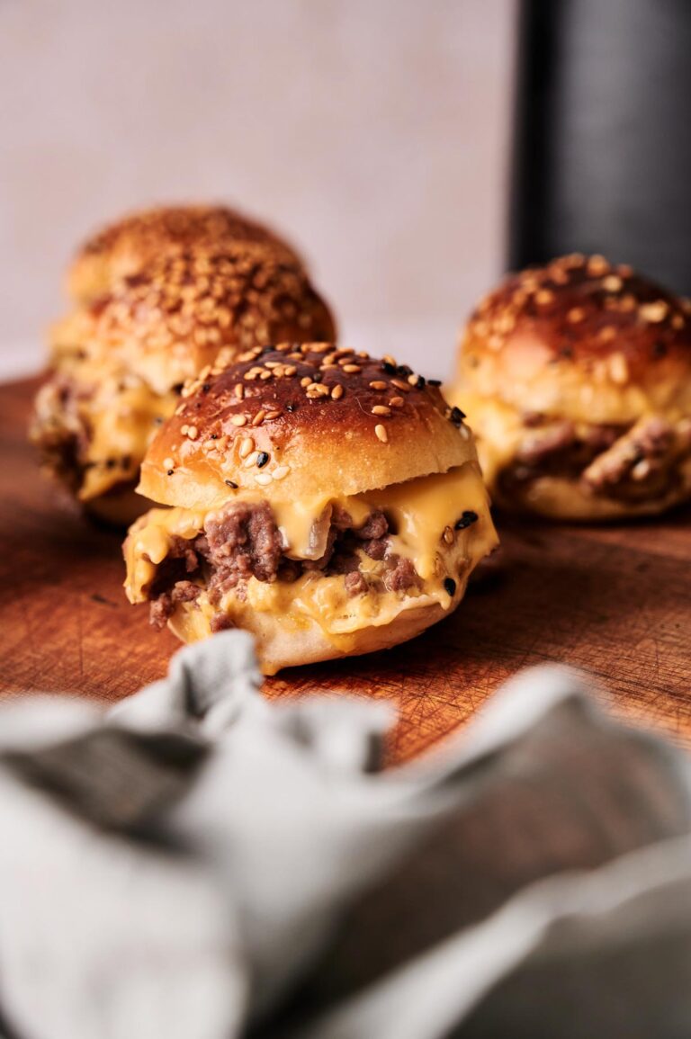 Three cheeseburgers with sesame seed buns and melted cheese are arranged on a wooden surface, perfect for serving as Air Fryer Hamburger Sliders at your next gathering.